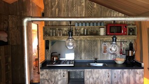 A rustic kitchen with wooden walls, a gas stove, a sink, a microwave, and various kitchen utensils. - Homely Tent with Kitchen & Shower near Beach & Campsite ('s-Gravenzande)