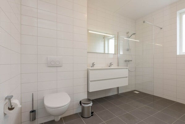 A modern bathroom with a toilet, sink, mirror, and shower. - Apartment in Zoutelande Near Sunny Beach (Zoutelande)