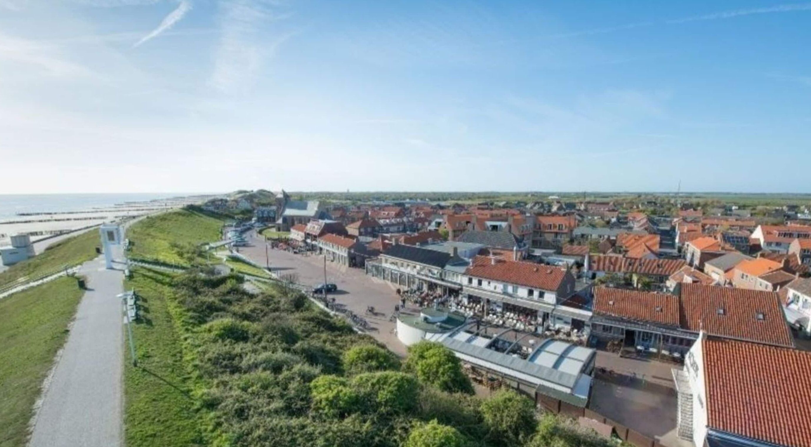 A coastal town with a promenade, traditional buildings, and a fortification on a hill.
