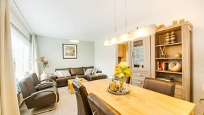 A modern living room with a dining area, featuring a wooden dining table, black leather chairs, a sofa, and a bookshelf. - Holiday Home in Kilder Near Bergherbos (Kilder)