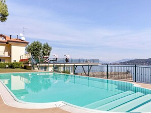 Ein Pool mit Meerblick, eine überdachte Terrasse mit Liegestühlen und ein Gebäude mit Balkonen.