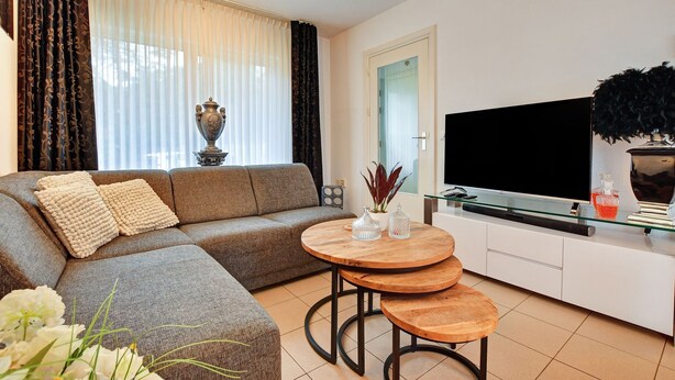 Un salon moderne avec un canapé, une table basse et un téléviseur posé sur un meuble blanc.