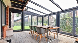 Une véranda avec un toit en verre, une table en bois et des chaises.