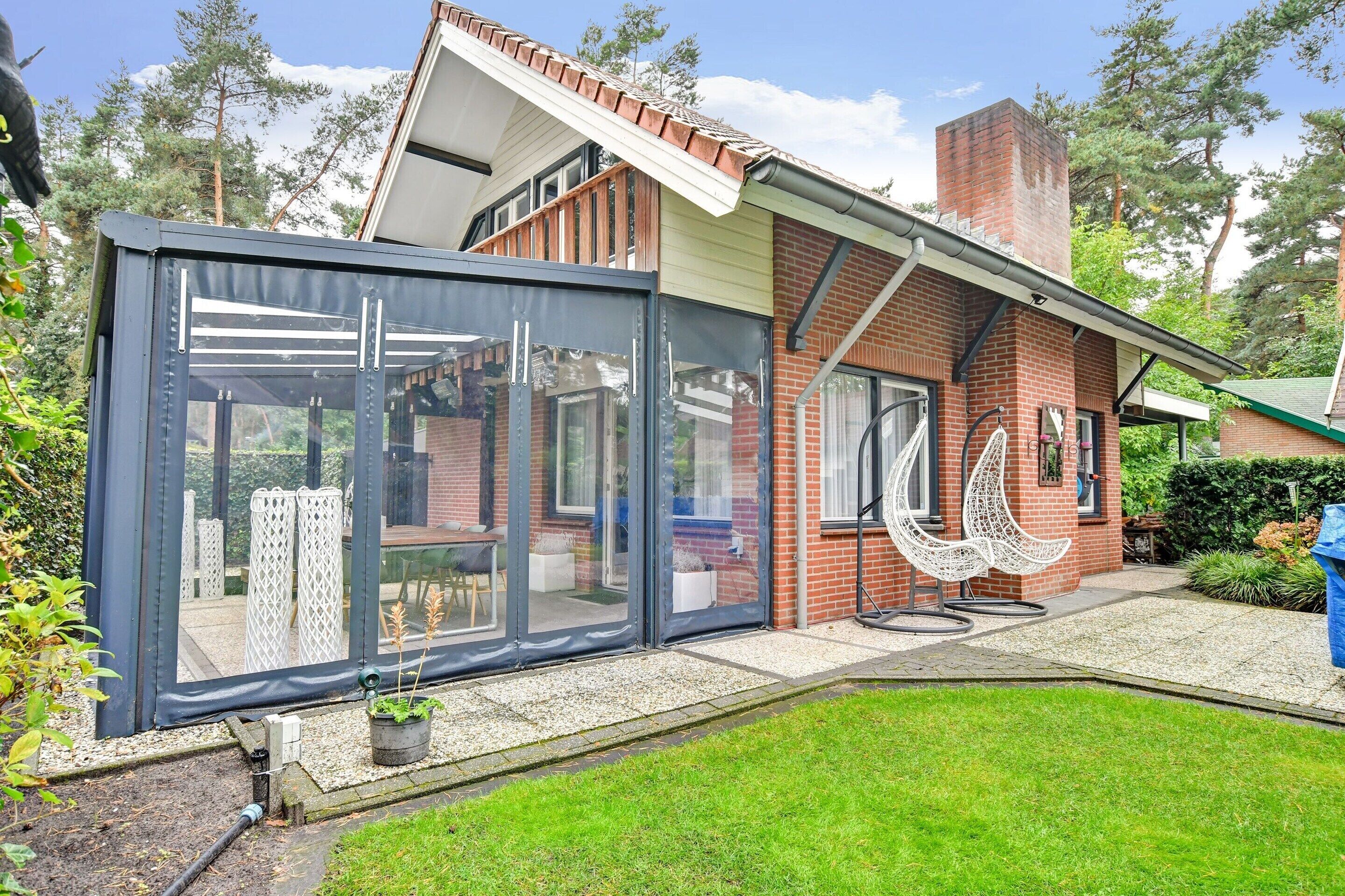 A modern house with a glass enclosure, brick exterior, and a small garden.