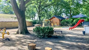 Une aire de jeux avec un toboggan, des balançoires et un petit abri en bois.