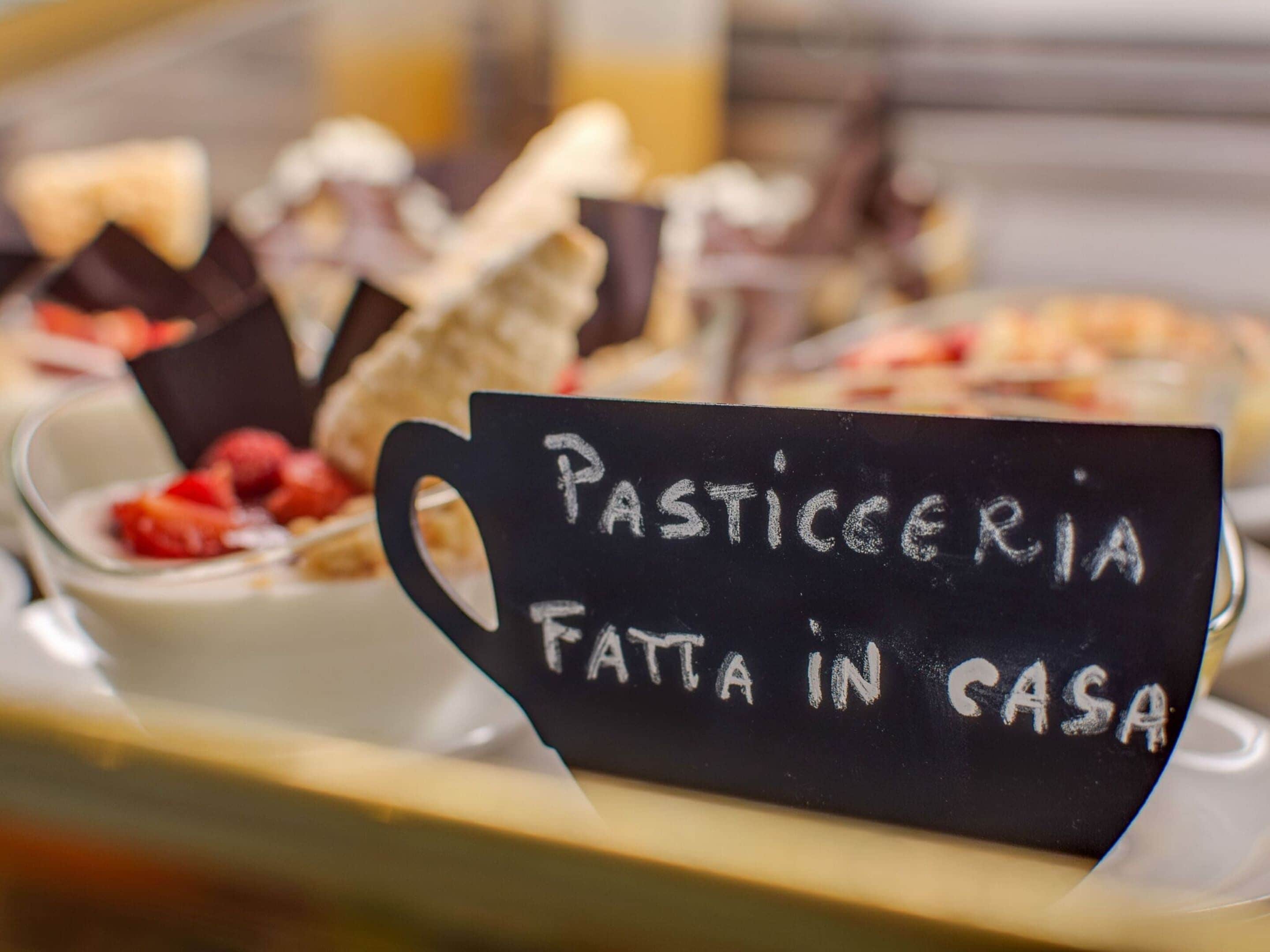 Exposição de sobremesas com uma placa que diz 'Pasticceria Fatta in Casa'.