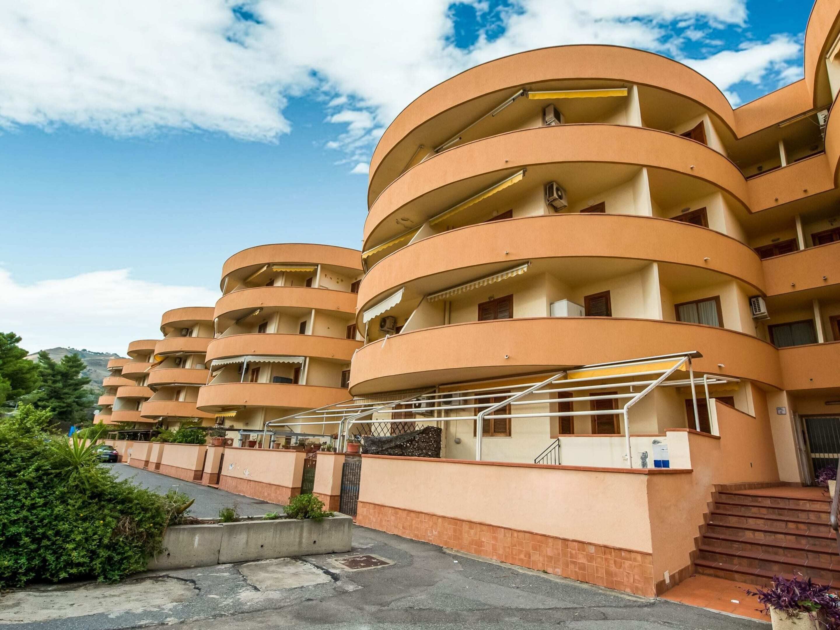 Un immeuble à plusieurs étages, doté d’une façade incurvée, de balcons et d’un escalier menant à l’entrée.