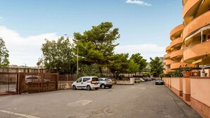 A parking area with several cars, a gated entrance, and a building with balconies.