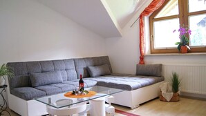 A modern living room with a grey sofa, a glass coffee table, and a window with orange curtains. - Delightful Apartment in Zell am Ziller With a View (Gerlosberg)