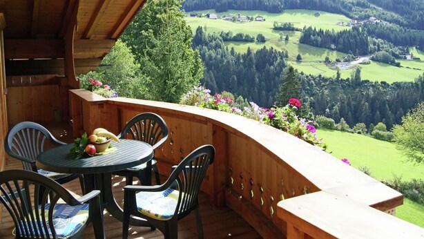A wooden deck with a table and chairs, overlooking a green valley with trees and buildings. - Delightful Apartment in Zell am Ziller With a View (Gerlosberg)