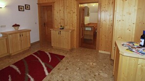 A wooden interior with a kitchen area, a dining table with magazines, and a red rug. - Delightful Apartment in Zell am Ziller With a View (Gerlosberg)