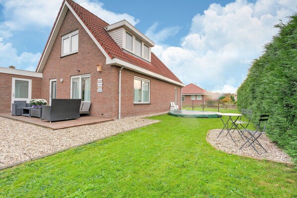 A two-story house with a sloped roof, a patio with outdoor furniture, and a well-maintained lawn.