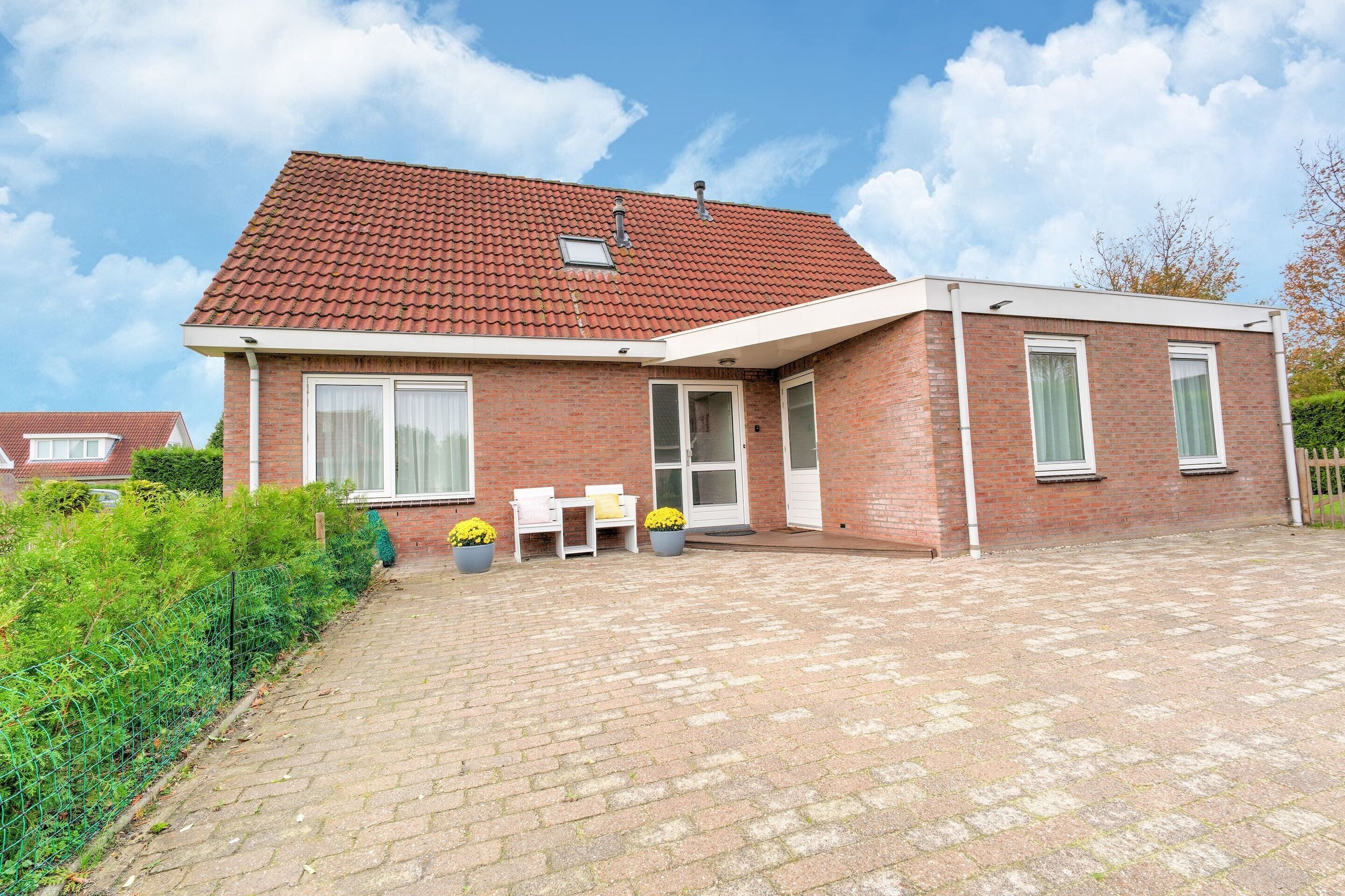 A two-story brick house with a tiled roof, a paved driveway, and a small patio with outdoor furniture.