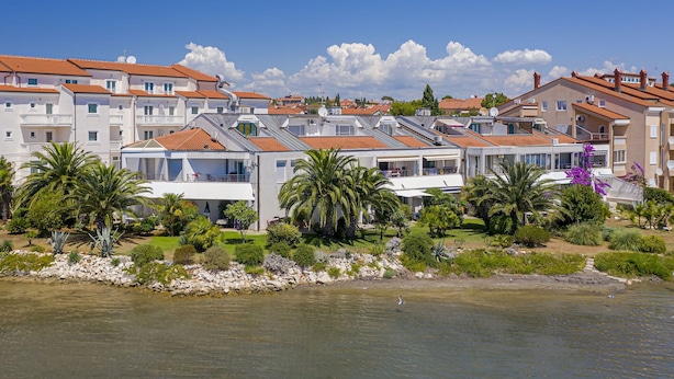 A coastal residential area with multiple two-story buildings, some with balconies, and a clear view of the sea. - Scenic Apartment With Garden in Medulin (Medulin)