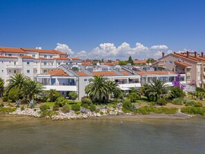 A coastal residential area with multiple two-story buildings, some with balconies, and a clear view of the sea. - Scenic Apartment With Garden in Medulin (Medulin)