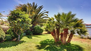 A well-maintained garden with various trees and shrubs, a clear sky, and a body of water in the background. - Scenic Apartment With Garden in Medulin (Medulin)