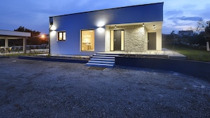 A modern two-story house with a stone facade, a covered patio, and a well-lit entrance. - Comfortable, Stylish, Detached Villa With Garden, Private Pool, Near the Beach (Medulin)