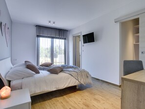 Un dormitorio moderno con cama, mesita de noche y televisor montado en la pared.