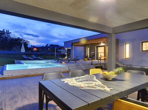 An outdoor patio with a pool, lounge chairs, and a dining table with a bowl of fruit.