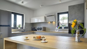 A modern kitchen with a central island, built-in appliances, and large windows. - Comfortable, Stylish, Detached Villa With Garden, Private Pool, Near the Beach (Medulin)