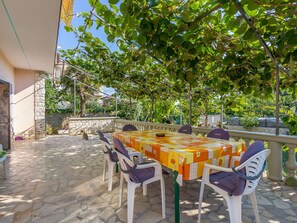 Um pátio externo com uma mesa e cadeiras, cercado por piso de pedra e vegetação.
