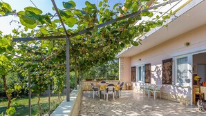 A covered outdoor patio with stone flooring, a pergola with climbing plants, and a seating area with tables and chairs. - Alluring Apartment in Medulin near Beach (Medulin)