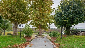 A paved pathway flanked by large trees and potted plants, leading to a covered area with a view of a distant landscape. - Cozy Tuscan Getaway (Fucecchio)