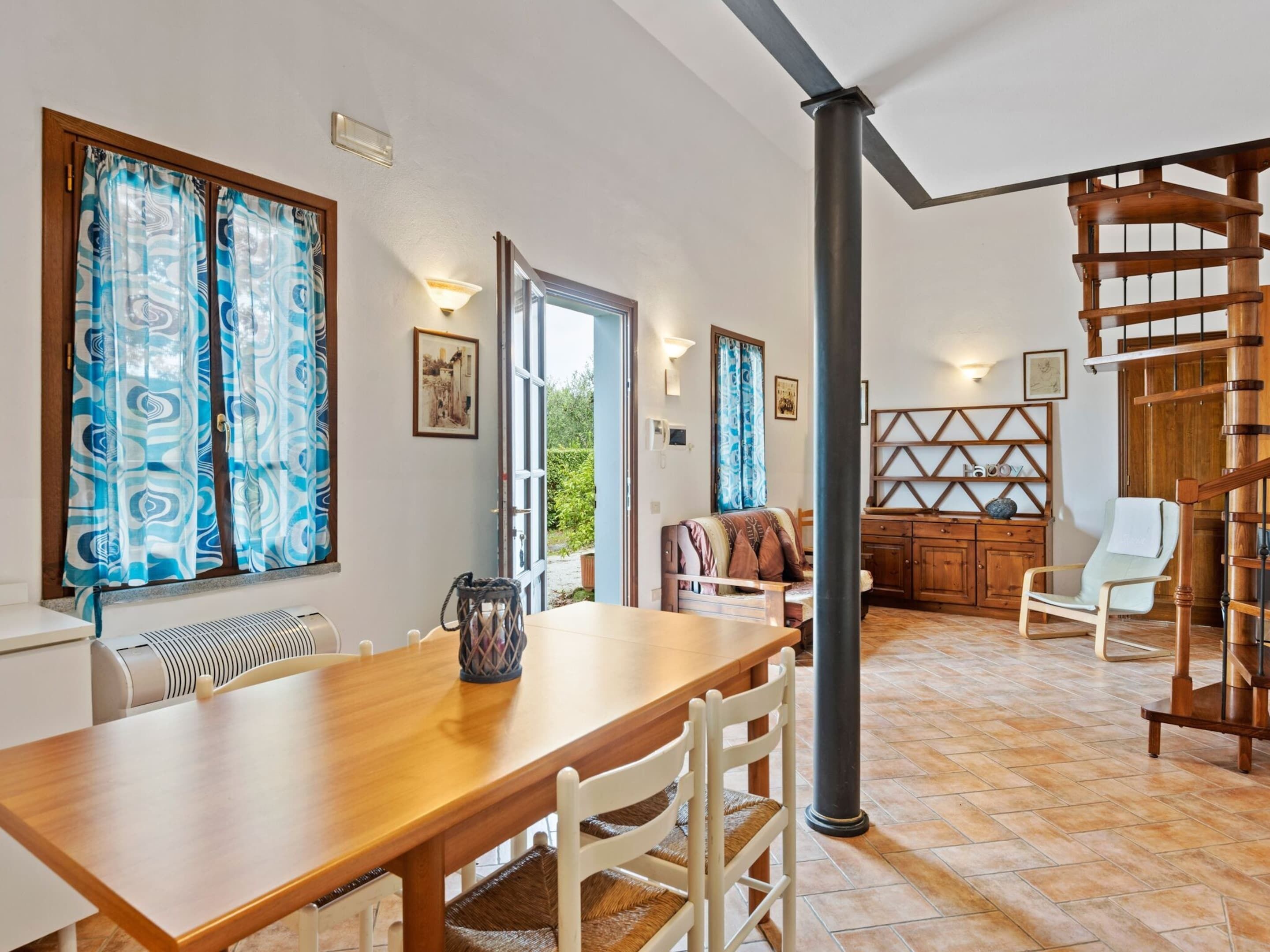A spacious living area with a wooden dining table, white chairs, a sofa, and a staircase.