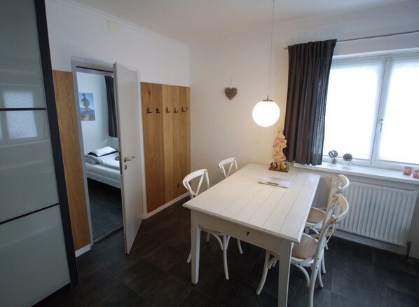 A compact room with a dining table, chairs, a bed, and a window with curtains.