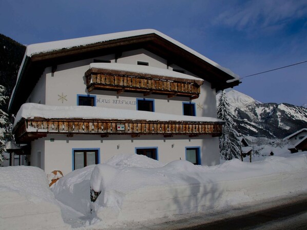 A two-story building with a snow-covered roof and balconies, surrounded by snow and mountains. - Fabulous Apartment in Bichlbach (Bichlbach)