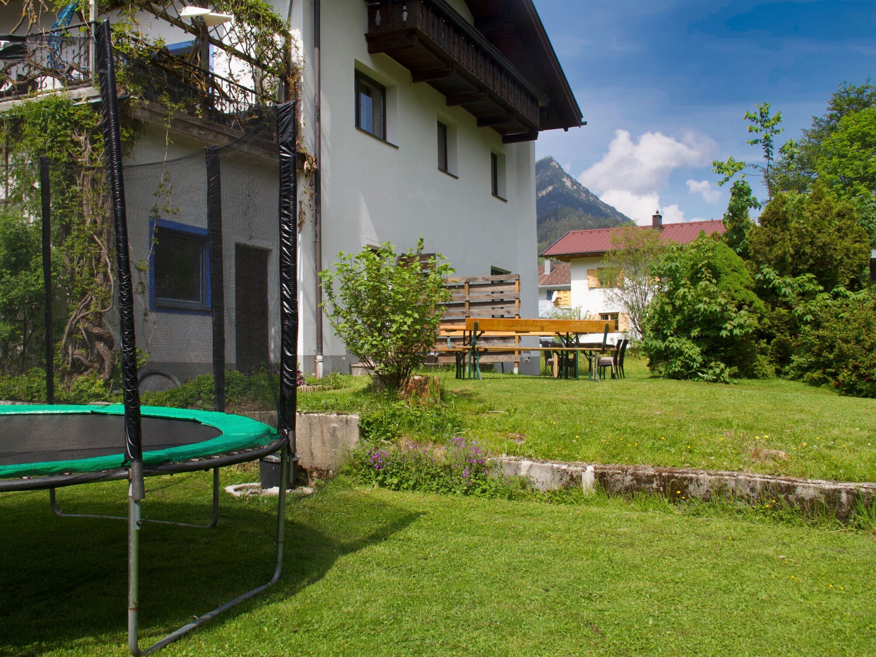 A house with a trampoline in the yard, a wooden bench, and a mountain in the background.