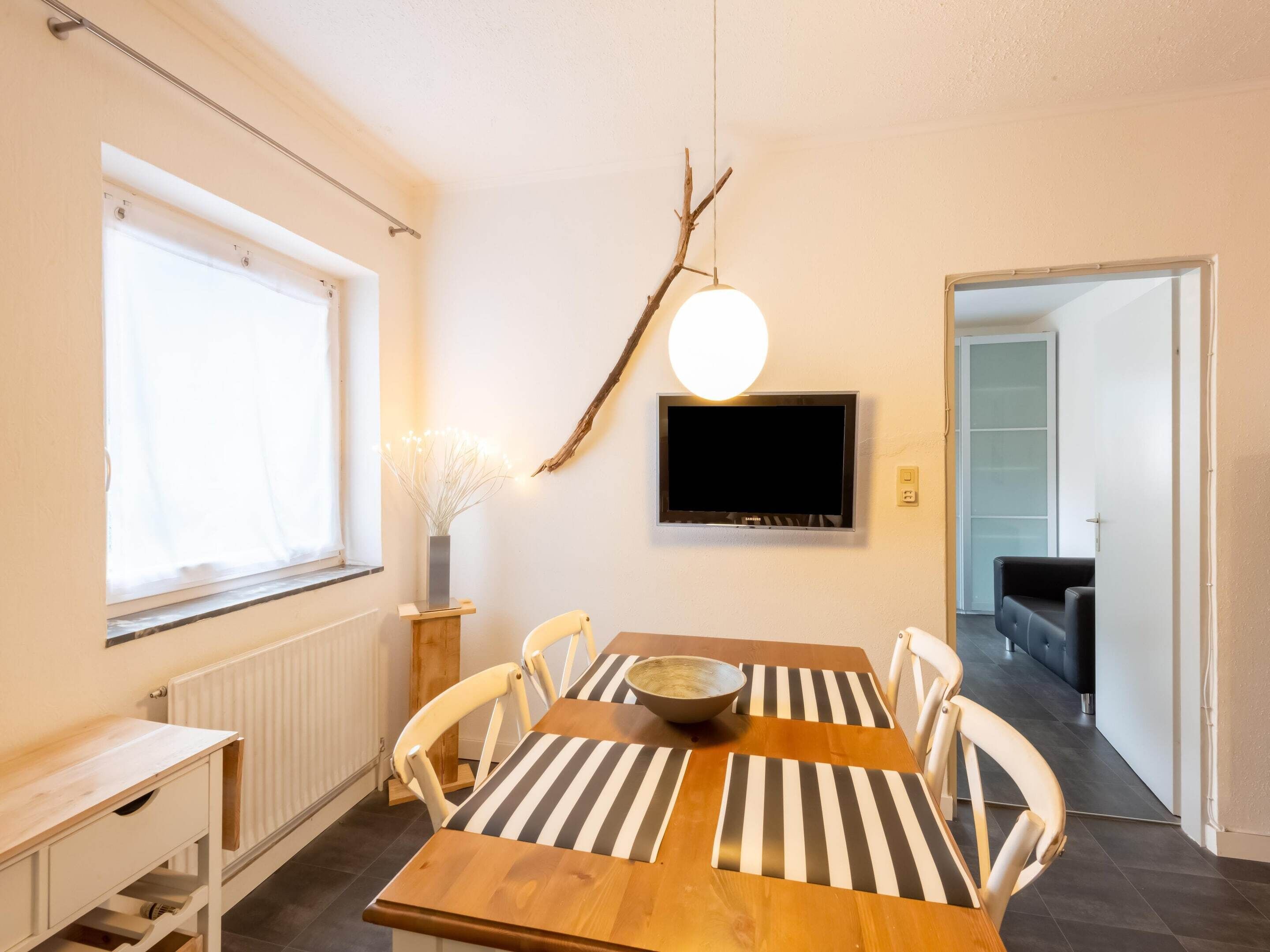A dining area with a wooden table, striped cushions, a bowl, and a television on the wall.