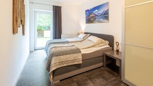A bedroom with a bed, a nightstand, a painting, and a view of the outdoors.