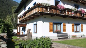 A traditional Alpine-style building with wooden balconies, stone steps, and flower boxes.