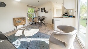 A modern kitchen with white cabinets, a dining area with a round table, and a large window. - Nice Chalet With Dishwasher, Near Efteling (Kaatsheuvel)