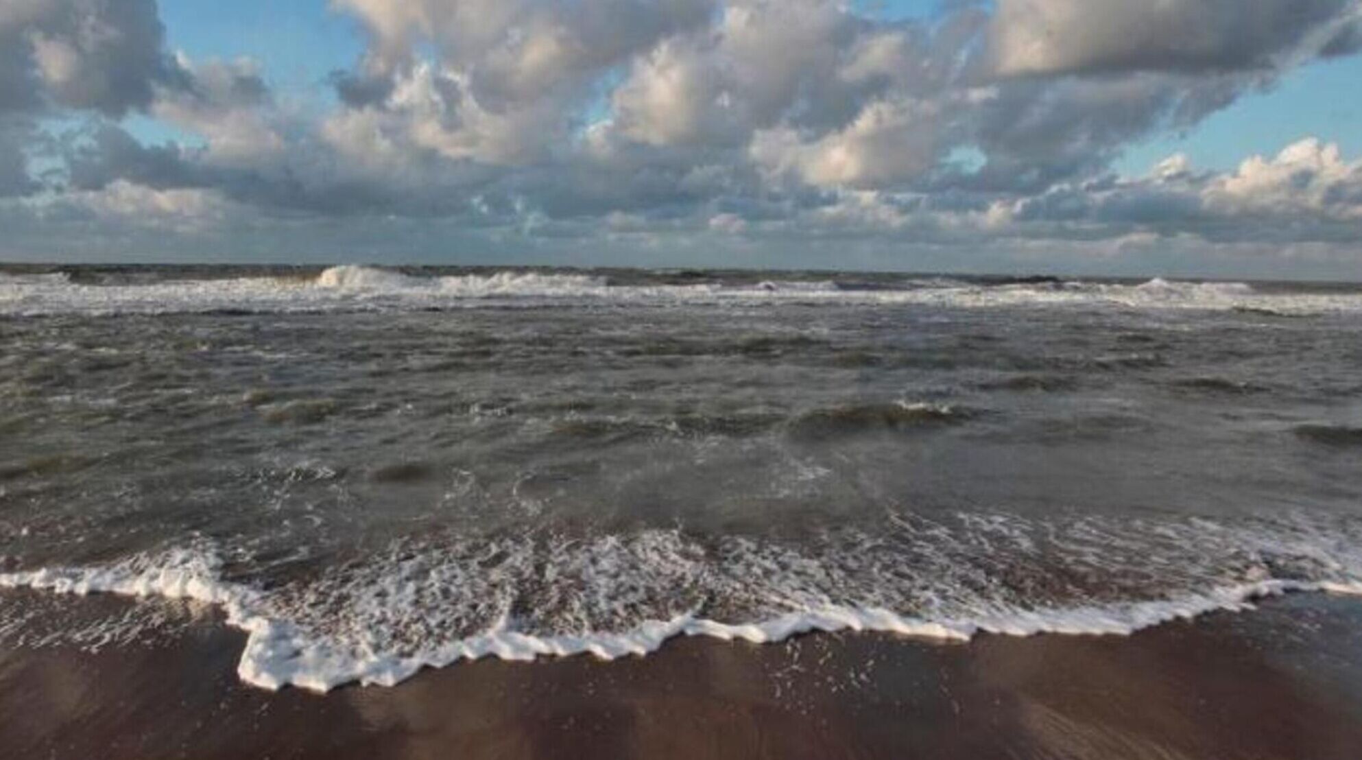 A beach with waves crashing onto the shore and a partly cloudy sky.