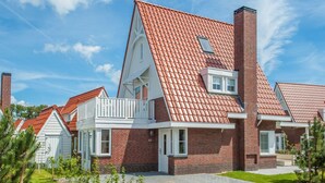 A modern residential building with a red-tiled roof, brick exterior, and a well-maintained lawn. - Luxury Villa near Sea (Kamperland)