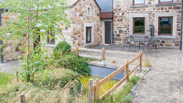 A stone building with a wooden deck, a small pond, and a wooden fence.