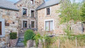 A stone building with a courtyard, steps leading to the entrance, and a small garden area.