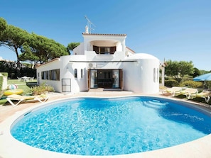A modern villa with a swimming pool, a patio with lounge chairs, and a garden with trees. - Modern Holiday Home in Quarteira With Swimming Pool (Loulé)