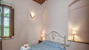 A bedroom with a wooden ceiling, a bed with a blue duvet, two bedside lamps, and a window with a view of trees. - Farmhouse in Monticiano Near Petriolo Spa (Monticiano)