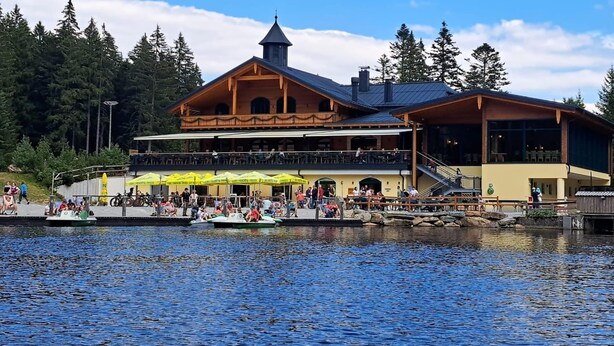 A lakeside lodge with a large dining area, outdoor seating, and a boat dock. - Sunny, Modern Furnished Apartment Your Favourite Place to Relax (Viechtach)