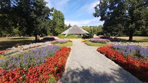 A garden pathway leading to a gazebo with a tiled roof, surrounded by vibrant flower beds. - Sunny, Modern Furnished Apartment Your Favourite Place to Relax (Viechtach)