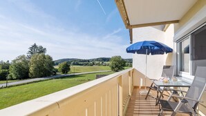 A balcony with a table and chairs, a blue umbrella, and a view of a green landscape. - Sunny, Modern Furnished Apartment Your Favourite Place to Relax (Viechtach)
