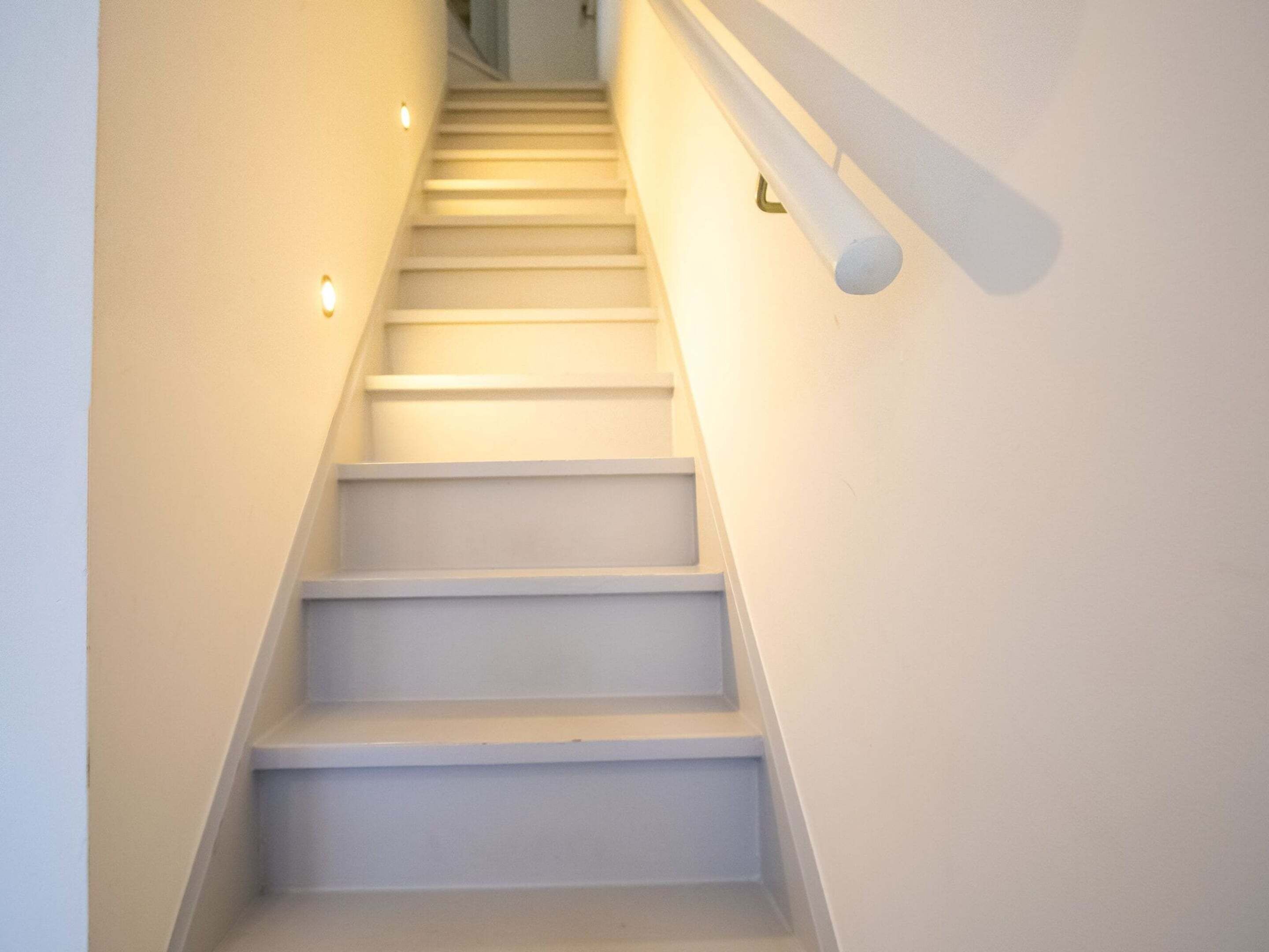 Un escalier avec des marches et des rampes blanches, menant à un palier.