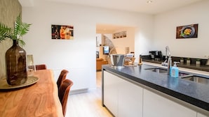 A modern kitchen with a central island, a dining area with a wooden table and chairs, and a view into the living area. - Elegant Holiday Home in Nieuwpoort near Beach (Nieuwpoort)