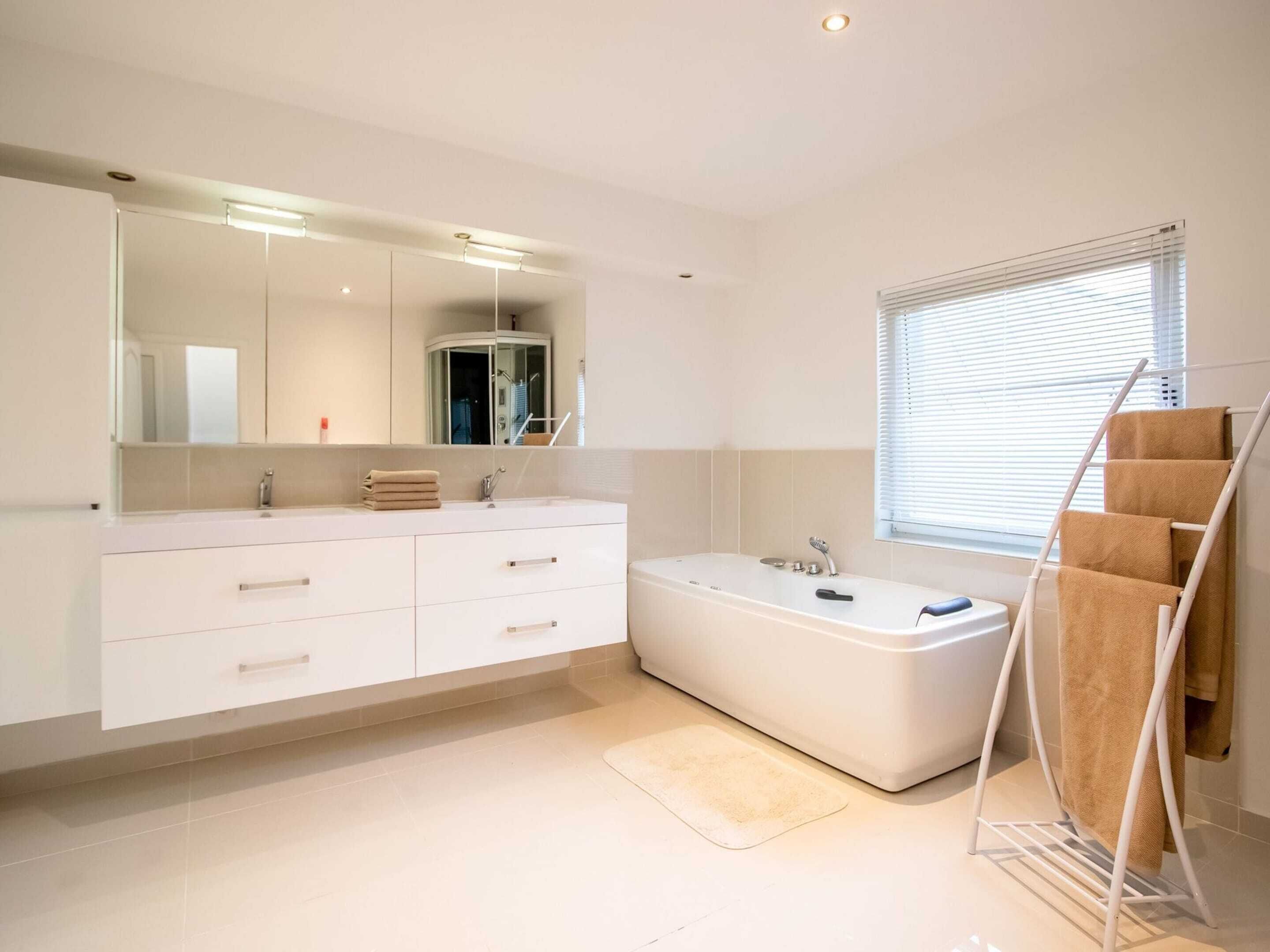 Une salle de bain moderne avec un grand miroir, un meuble-lavabo blanc, une baignoire et un porte-serviettes.