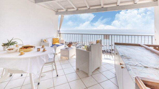 A covered outdoor area with a table set for dining, wicker furniture, and a view of the sea. - Sprawling Apartment in Cala Gonone near Cala Fuili Beach (Dorgali)