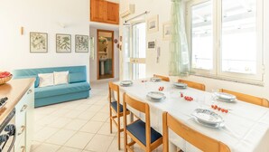 A bright kitchen with a dining table set for four, a blue sofa, and a wooden cabinet. - Sprawling Apartment in Cala Gonone near Cala Fuili Beach (Dorgali)