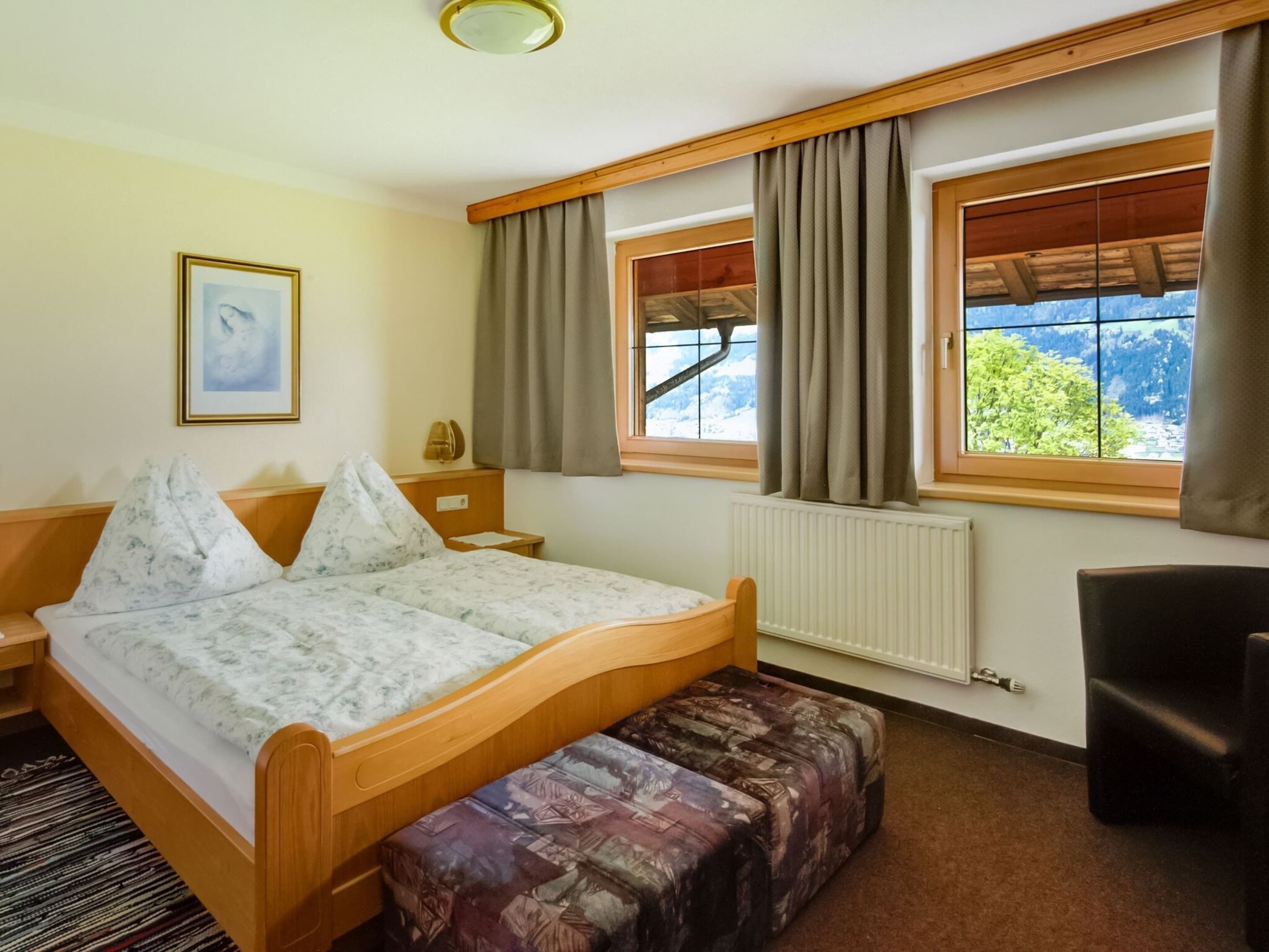 A bedroom with a wooden bed, a bench, a desk, and a window with curtains.